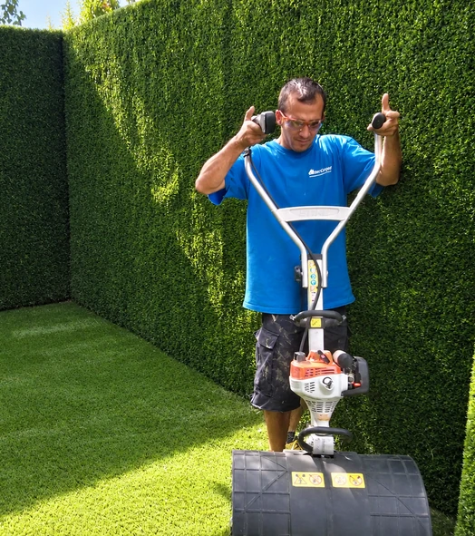 Operario cepillando césped artificial con una máquina en un jardín