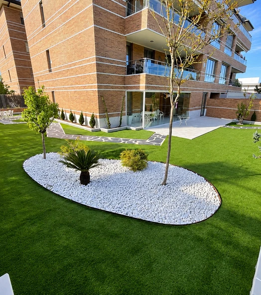 Jardín de chalet con césped artificial y árboles sobre un parterre de grava blanca